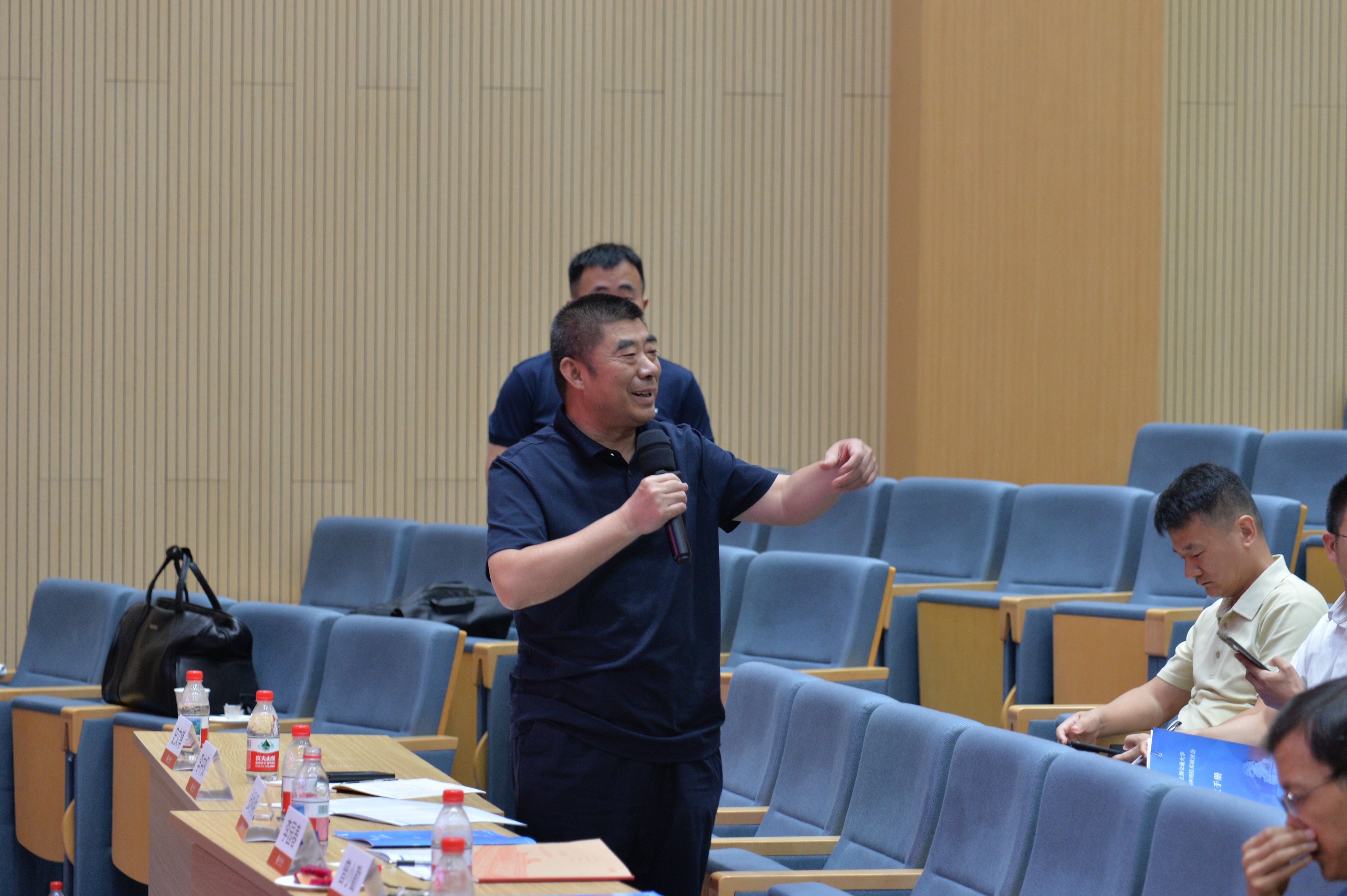 A person holding a microphone in front of a table

Description automatically generated